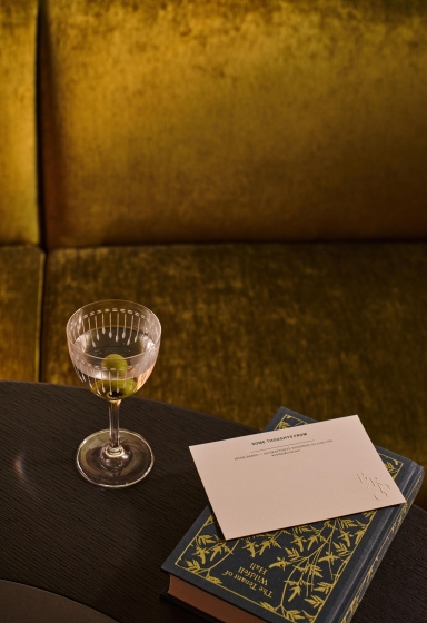 A martini glass with olives next to a stationary note and a book in Hotel Bardo