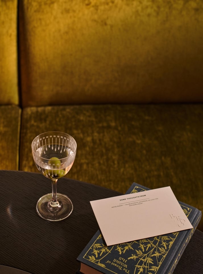 A martini glass with olives next to a stationary note and a book in Hotel Bardo