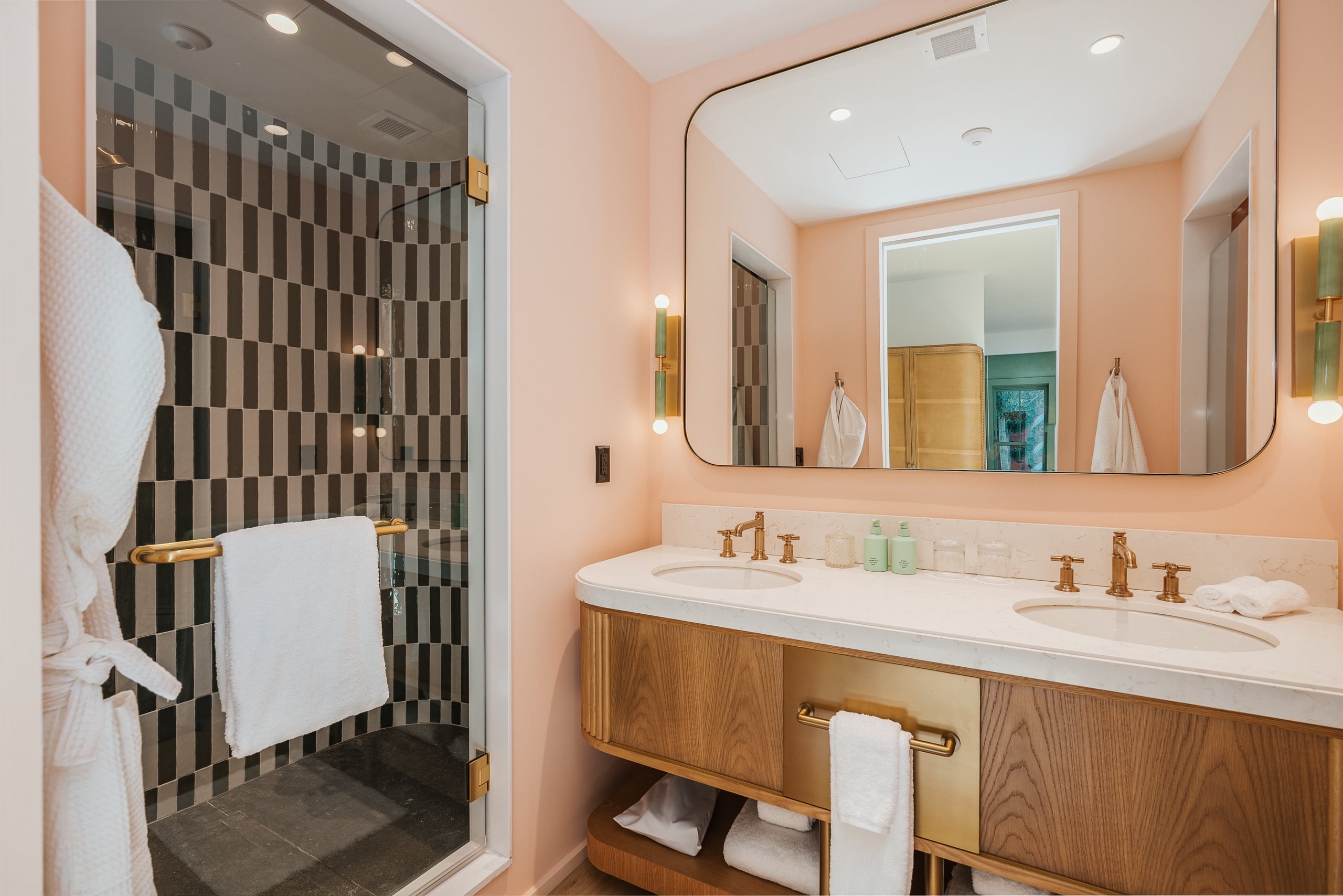 A bathroom with a double sink, a shower, and a mirror