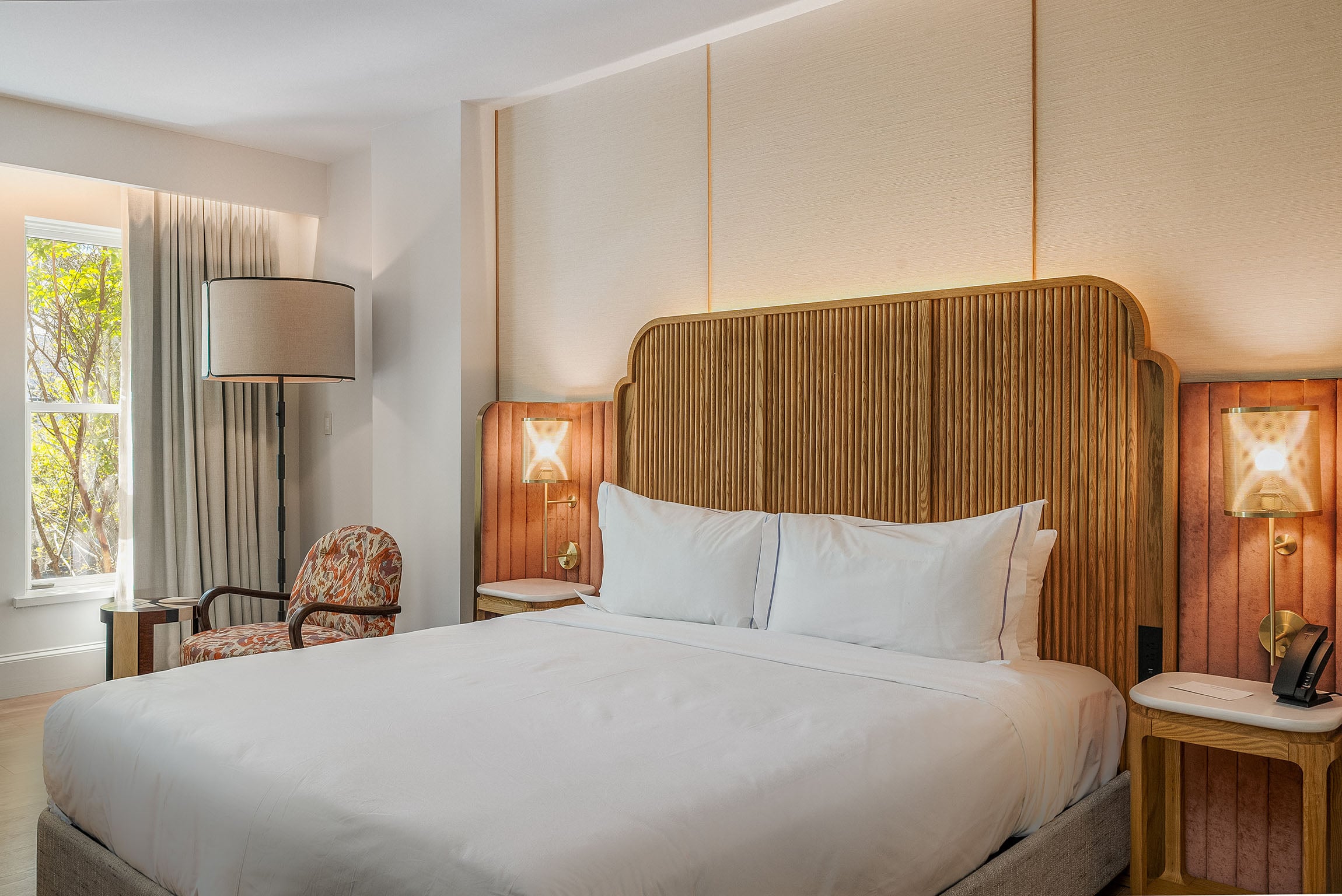 A hotel room with a large bed, wooden headboard, and modern furniture.