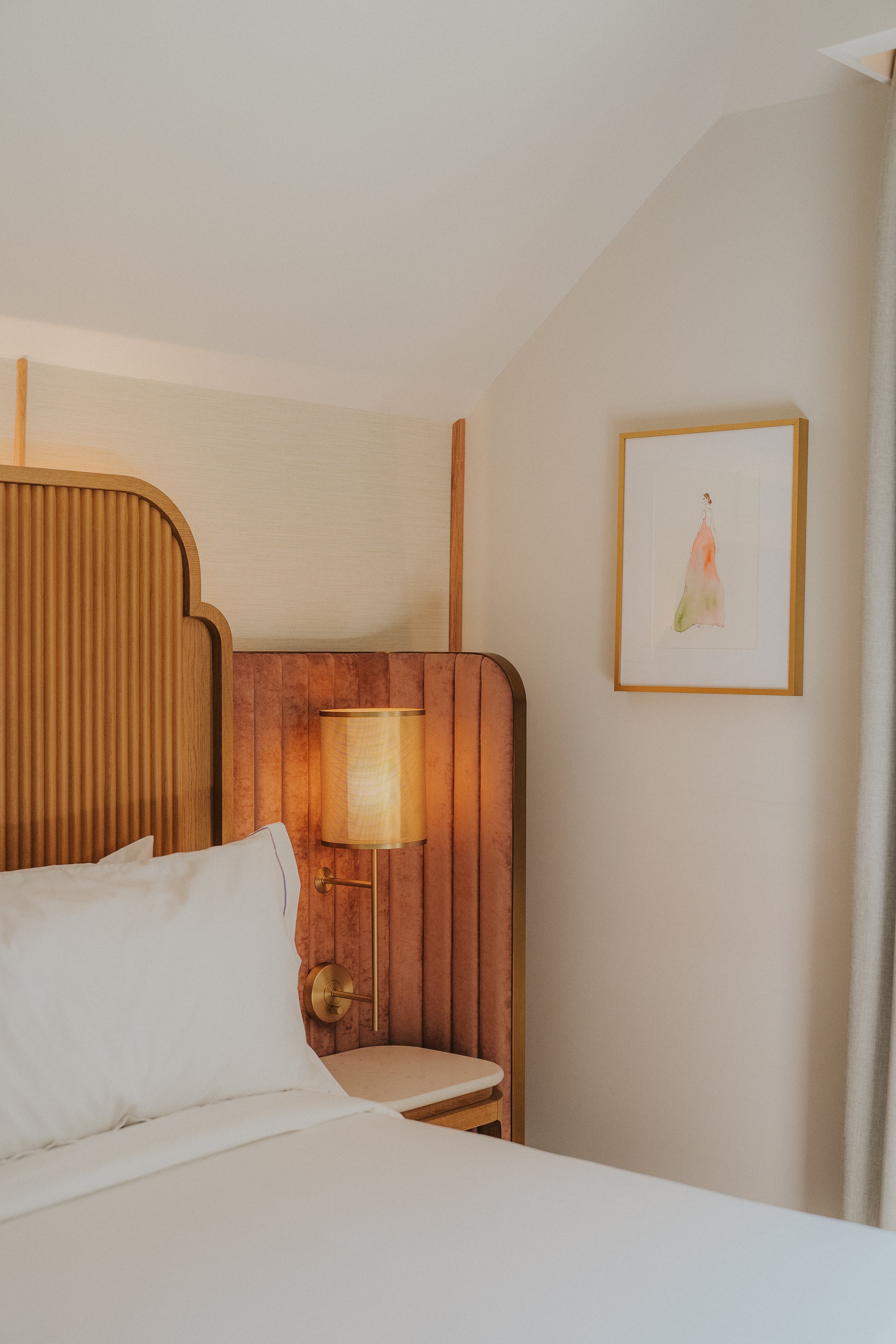 A close-up of a bed with a wooden headboard, a reading light, and a framed piece of artwork on the wall.