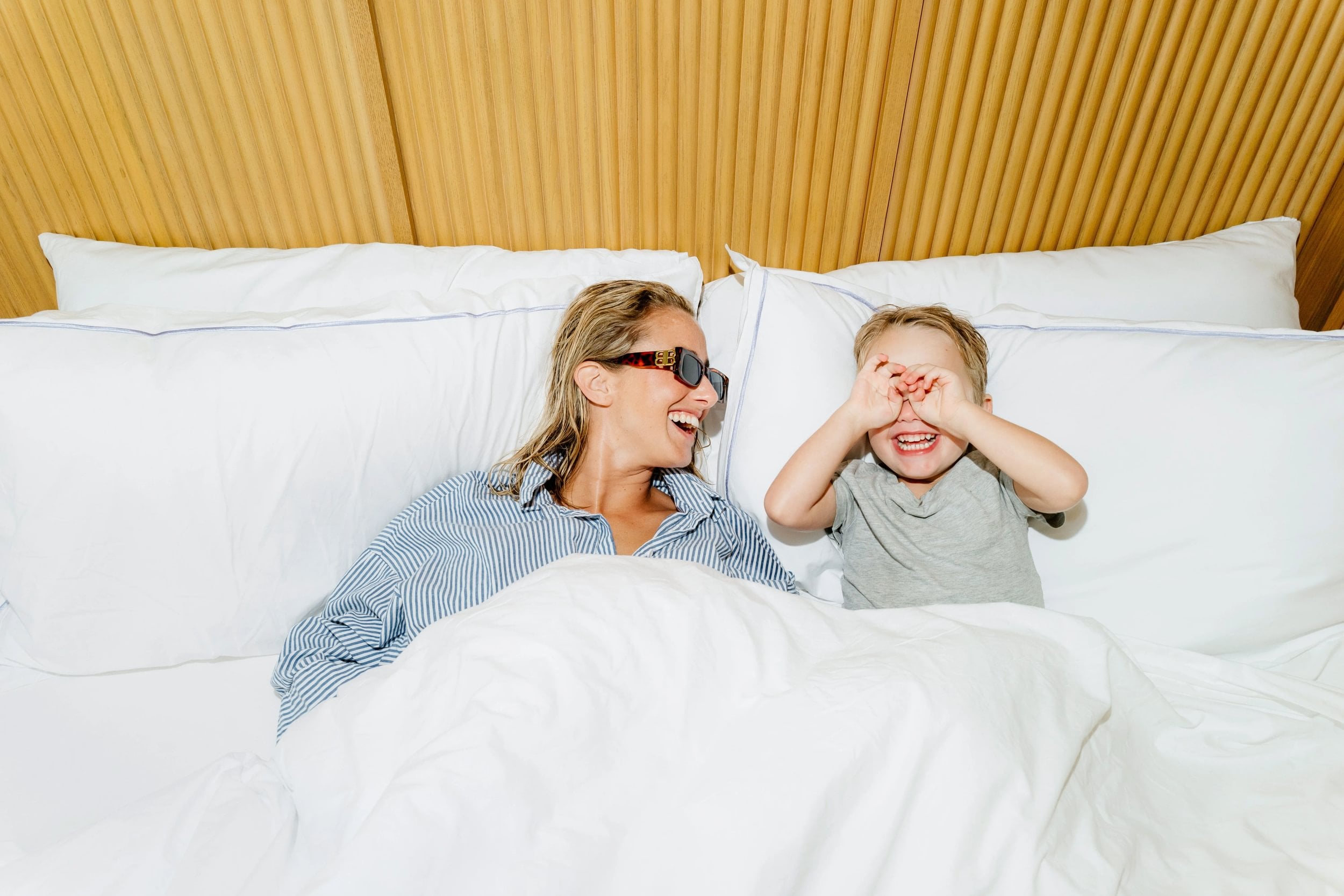 A woman and a child are lying in bed, smiling and covering their eyes.