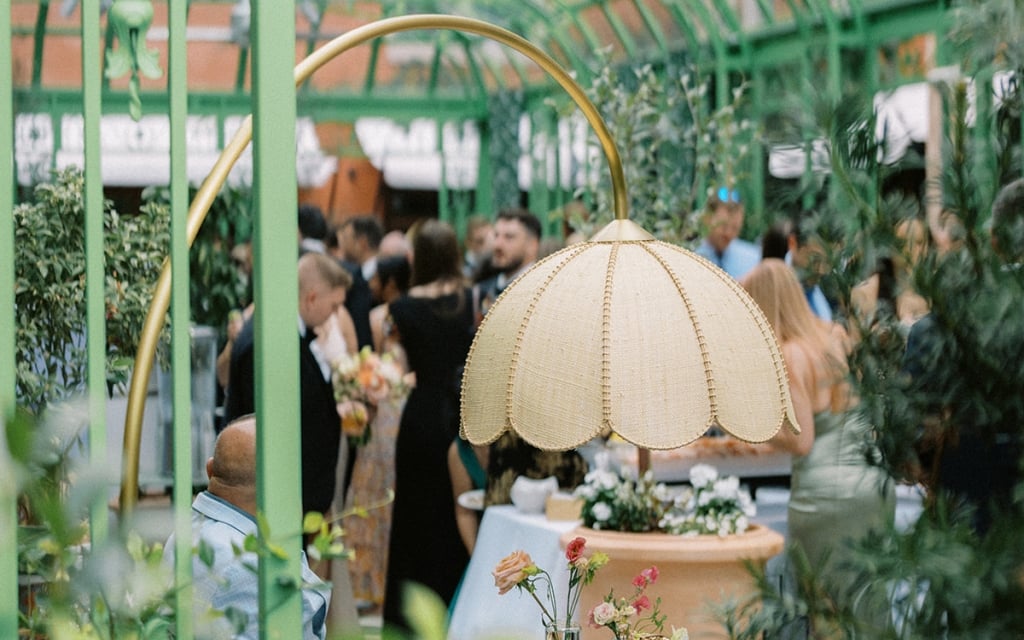 a group of people at tables under umbrellas in a green outdoor space