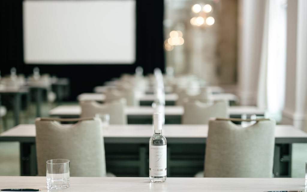 A meeting room with tables, chairs, bottles, and glasses.