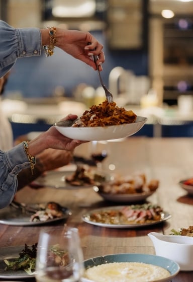 A person serving pasta on a table with various dishes and wine glasses.