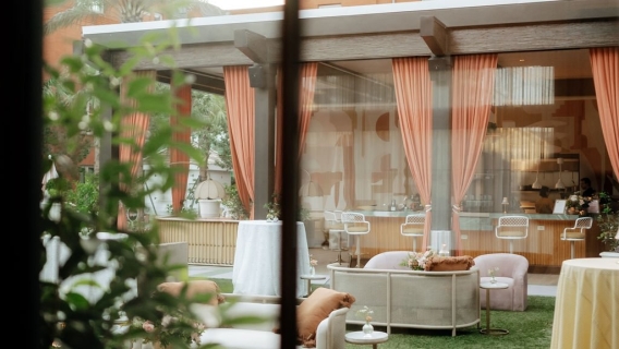 A view of an outdoor seating area with large windows, orange curtains, and furniture.