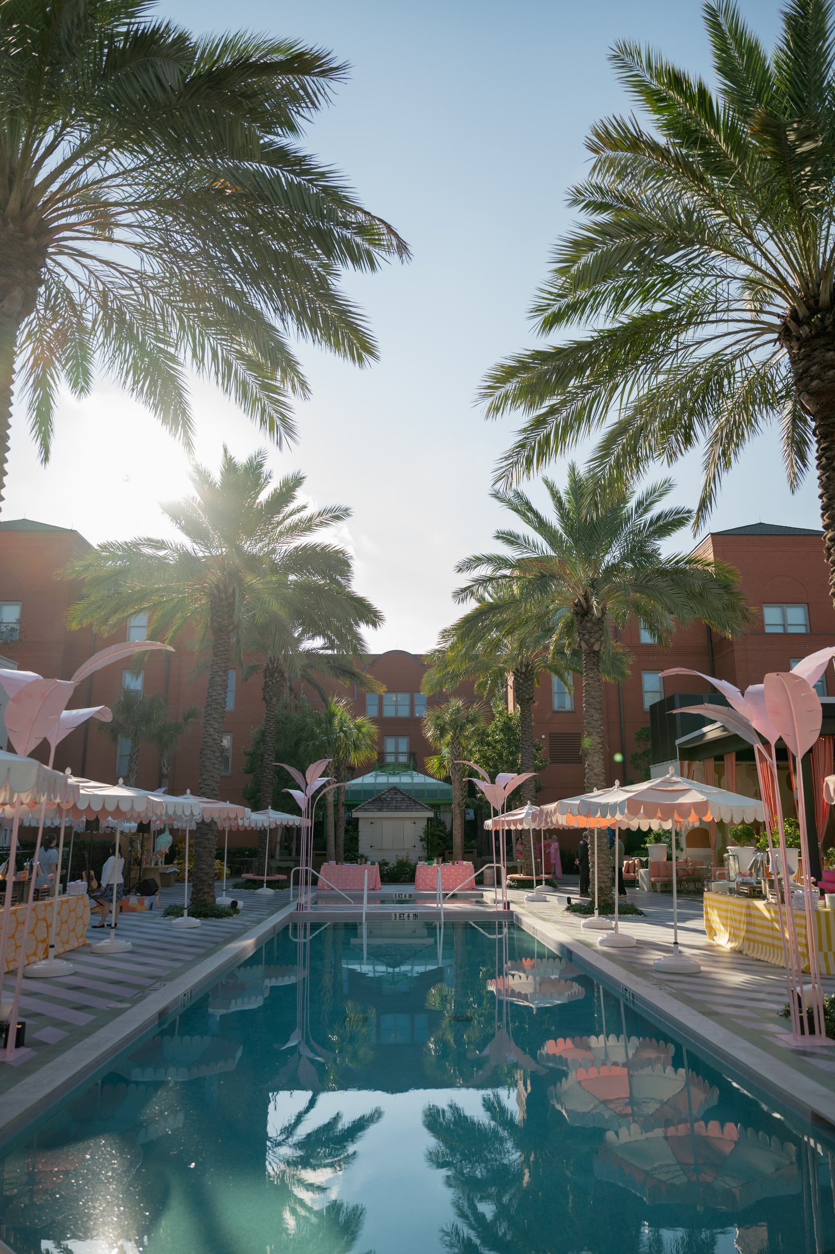 A hotel pool area with palm trees, umbrellas, and lounge chairs.