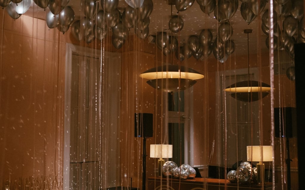 a room with silver balloons, chandeliers, and transparent curtains