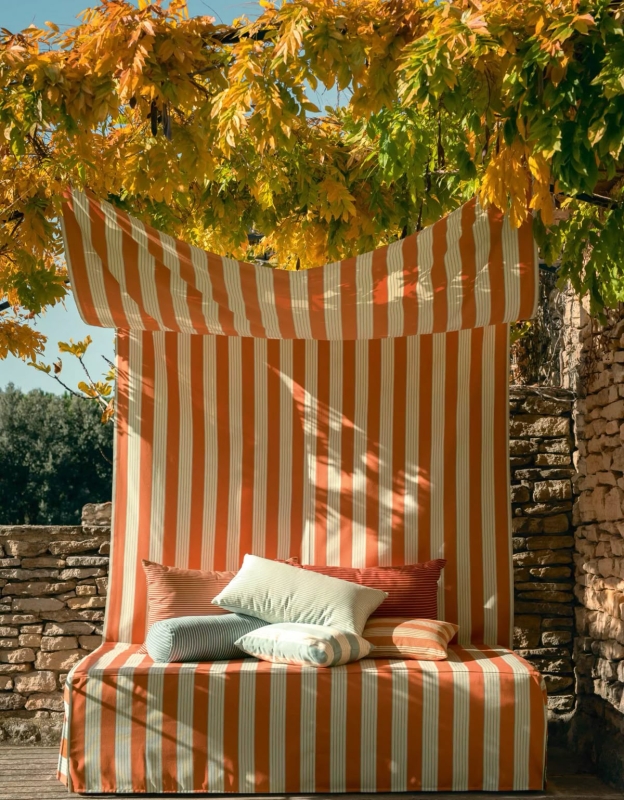 A orange and white stripped cabana furnished with many pillows